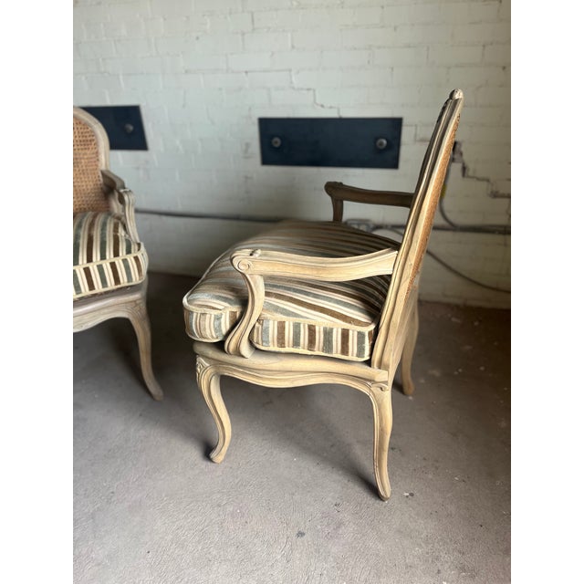 A charming pair of French Louis XV style bergère chairs featuring carved wood frames with a softly distressed finish,...