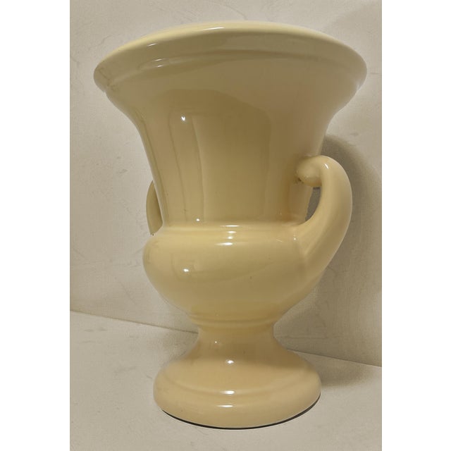 An understated vintage Neoclassical ceramic urn vase executed in a classic campana form. The vessel features a flared rim...