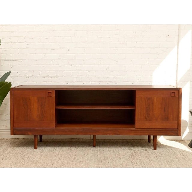 A handsome vintage teak credenza featuring a warm, rich wood finish and a beautifully streamlined silhouette. The design...