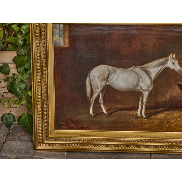 This English oil on canvas painting, dated 1884, captures the quiet elegance of a white horse standing in a dimly lit...