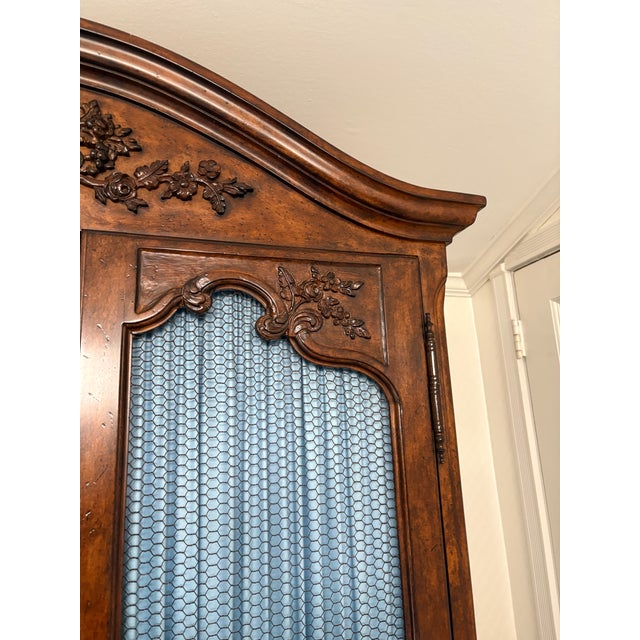 French provincial-Louis XV style armoire with a curved crown top, cabriole legs, and rich dark walnut finish. It features...