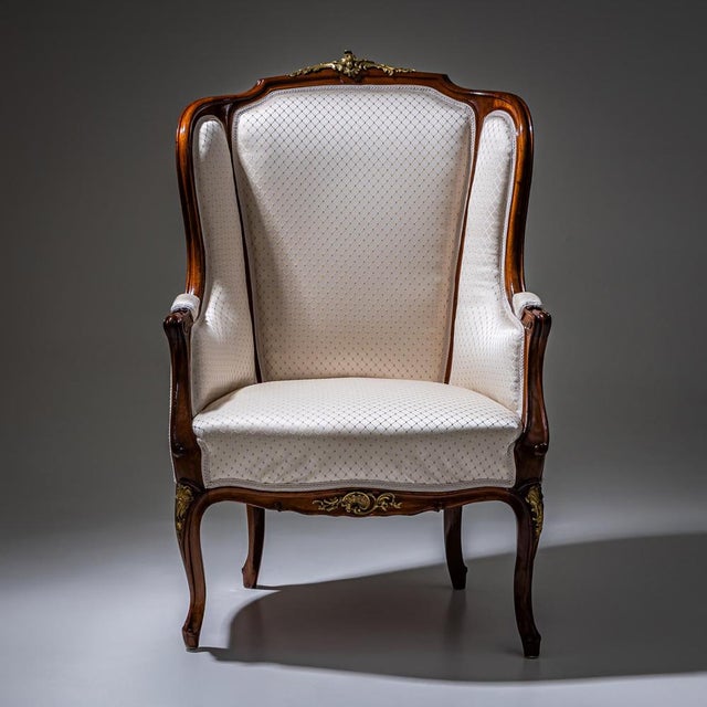 Louis XV style wingback armchair with Rococo-inspired bronze rocaille motifs along the frame. The chair is upholstered in...