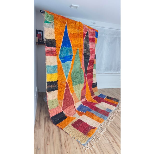 A vivid Boujaad patchwork — one half warm orange, the other deep burgundy and rose — crossed by a chain of four oversized...