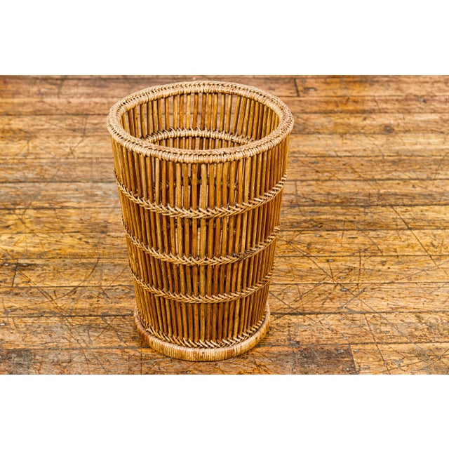 A Country style woven rattan waste basket with tapering lines. This vintage country-style woven rattan waste basket is a...
