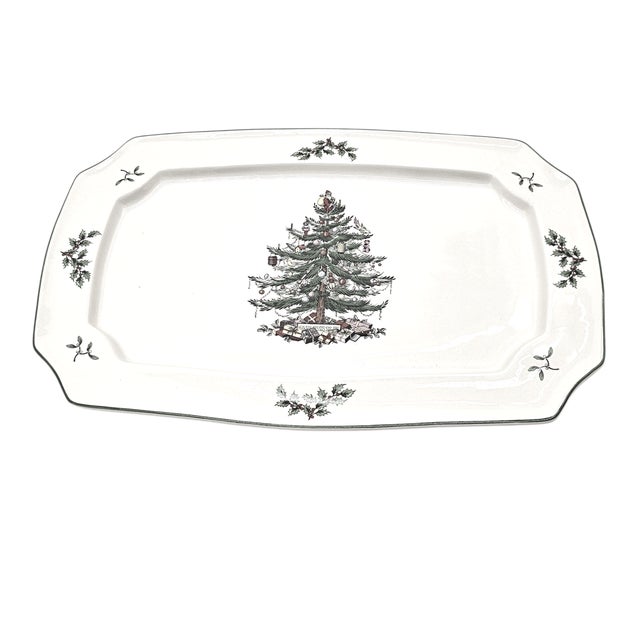 A pair of holiday platters, glazed ceramic, the tree evergreen and resolute. Presents scattered beneath, holly leaves...