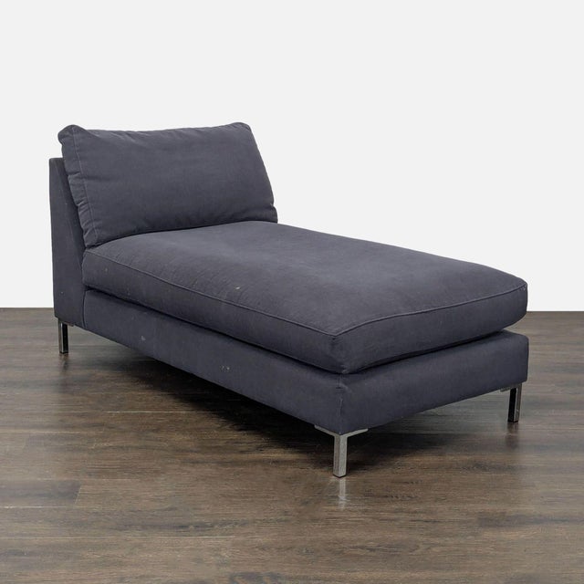 This CB2 chaise lounge offers a modern look with its clean lines and dark gray upholstery. It features a plush cushion and...
