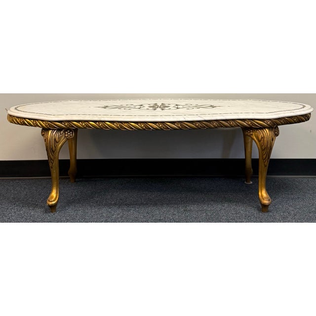 Elegant marble-top coffee table with a graceful shaped edge, soft gray veining, and a floral scroll motif framed by a...