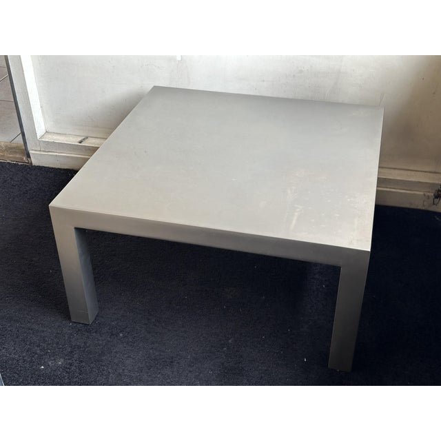 This large square coffee table is made of brushed stainless steel and follows a pared-back Parsons form. The top runs...