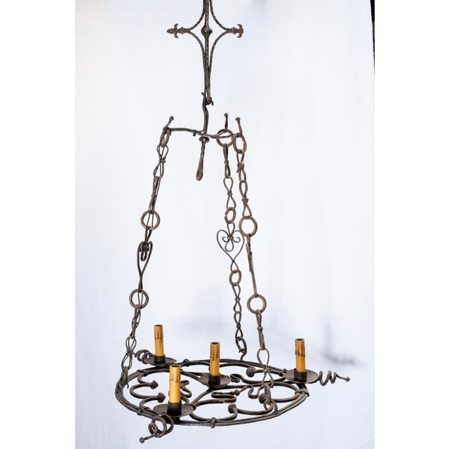 A circular, flat-base wrought iron chandelier, early 20th century, French. Base is suspended by 3 iron chains with...