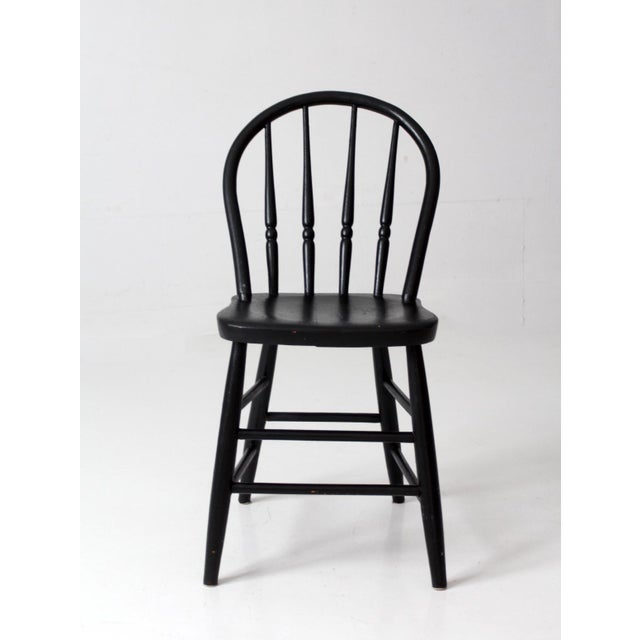 A vintage Windsor-style chair featuring a gracefully bowed back, turned spindles, and a shaped wooden seat, finished in...