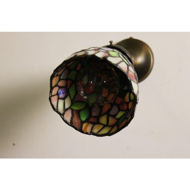 This Tiffany-style wall sconce is composed of stained glass in shimmering colors, soldered with tin. It is mounted on a...