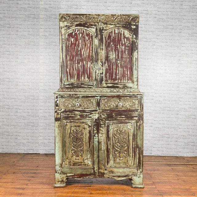 An Indian rustic painted wood cabinet from the early 21st century with carved scrolling foliage and distressed patina....