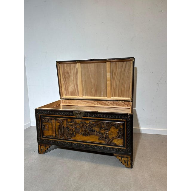 This beautifully detailed chest features intricate hand-carved panels depicting traditional oriental scenes with figures,...
