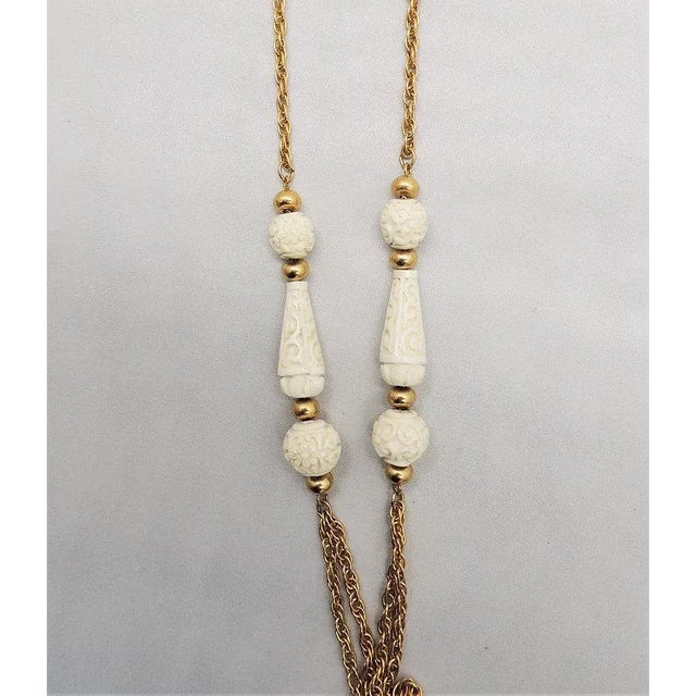 This is part of Chairish’s Costume Jewelry assortment. Early 1970s goldtone and resin faux-carved ivory sautoir necklace...