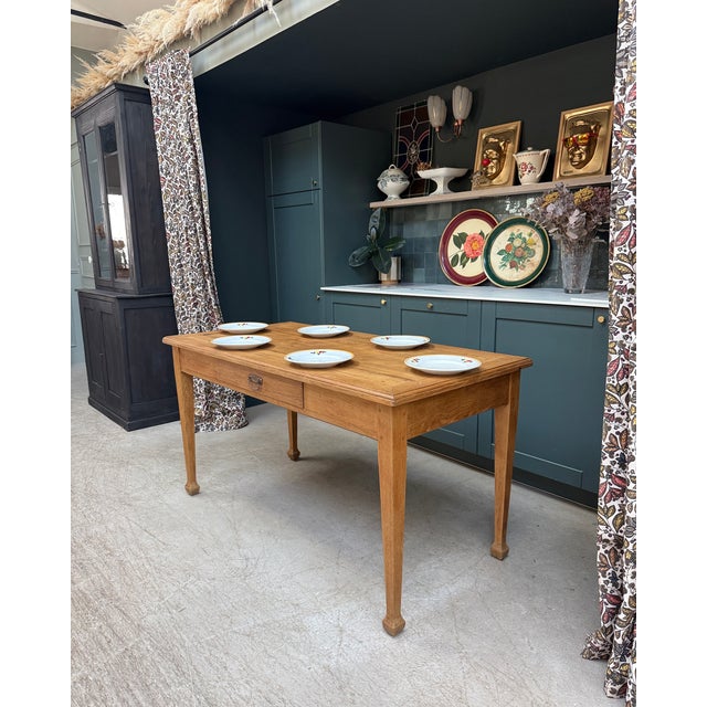 This antique country table in solid oak likely dates from the late 19th century. Its simple lines, slender legs, and warm...
