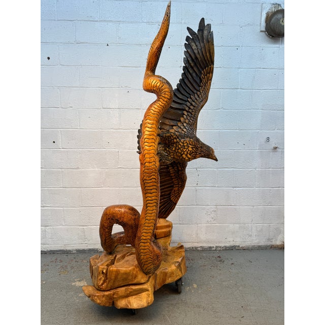 Make a striking statement with this large, hand-carved wooden sculpture depicting a soaring eagle intertwined with a tall...
