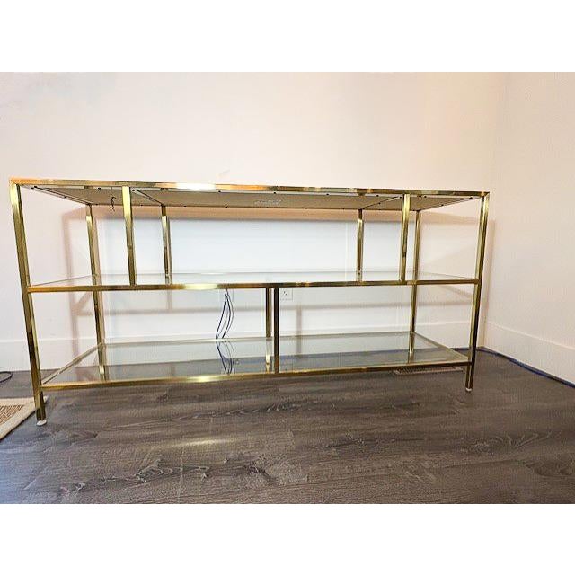 A mid-century modern inspired console table constructed with a brass frame, leather top and glass details. The geometric...