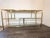 A mid-century modern inspired console table constructed with a brass frame, leather top and glass details. The geometric...