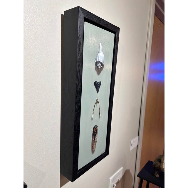This artwork features a vertical arrangement of natural objects, including a shell, a stone, twigs, and a cicada,...