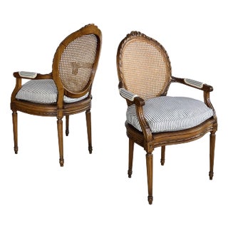 Pair of Early 1900s Louis XVI Style Carved Walnut Arm Chairs With Caned Back & Seat For Sale
