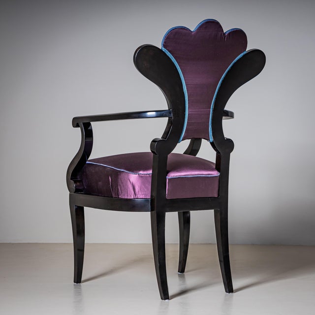 Ebonized armchair featuring a fan-shaped backrest and gracefully curved arm supports. The chair stands on tapering legs...