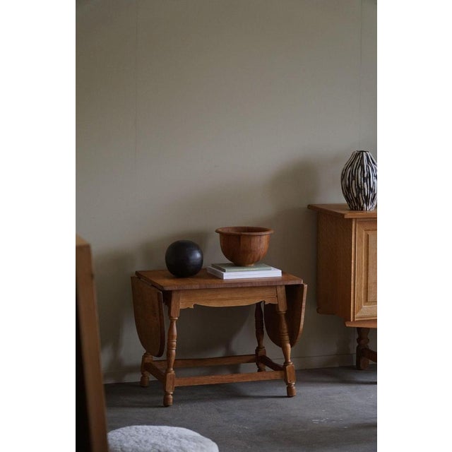 Presenting a neat folding side table in oak, made in the style of Henning Kjærnulf from the vibrant 1960s era. Crafted...