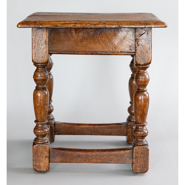 A superb antique 19th-Century English oak pegged joint stool with hand turned legs and beveled edge on the seat. It...