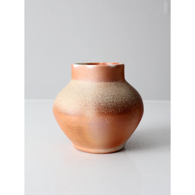A vintage handmade studio pottery vase featuring a softly rounded form and warm terracotta and clay tones that bring...