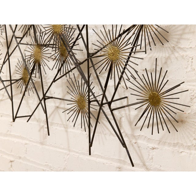 A dramatic metal wall sculpture composed of dozens of radiating starburst forms connected by slender branching rods. The...