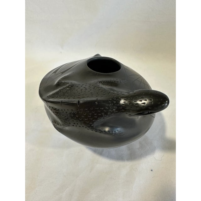 A lizard with detailed scales winds around the edge and raises its head up from the surface of this small black on black...