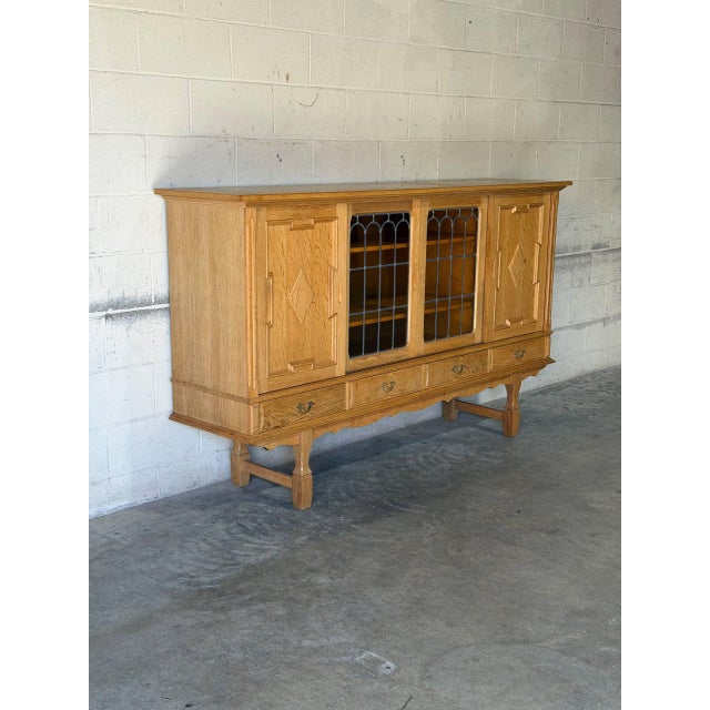 This high sideboard features sliding leaded glass doors flanked by carved outer panels. It rests on a trestle base with...
