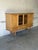 This high sideboard features sliding leaded glass doors flanked by carved outer panels. It rests on a trestle base with...