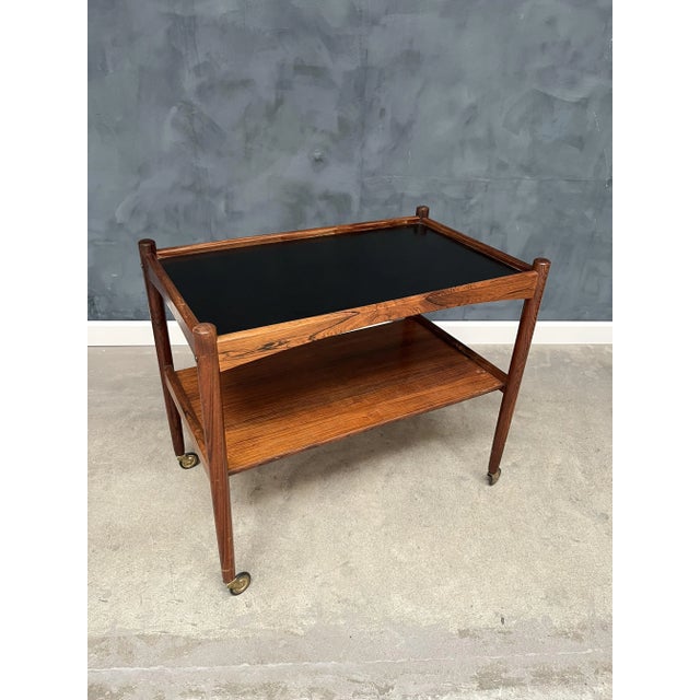 Charming rosewood rolling cart from the 1960s, featuring a sleek black Formica top. This stylish piece is both practical...