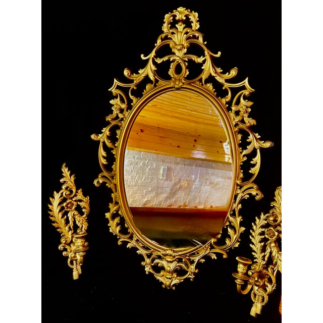 This elegant set features a large oval wall mirror with an ornate, gilded rococo-inspired frame, accompanied by two...