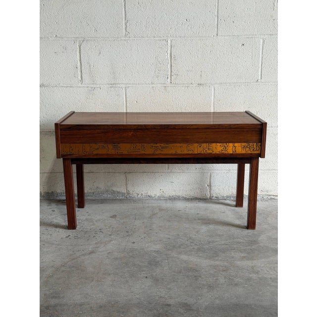 This exceptional accent piece features a minimalist rectangular tabletop sitting over a wide single storage drawer. The...