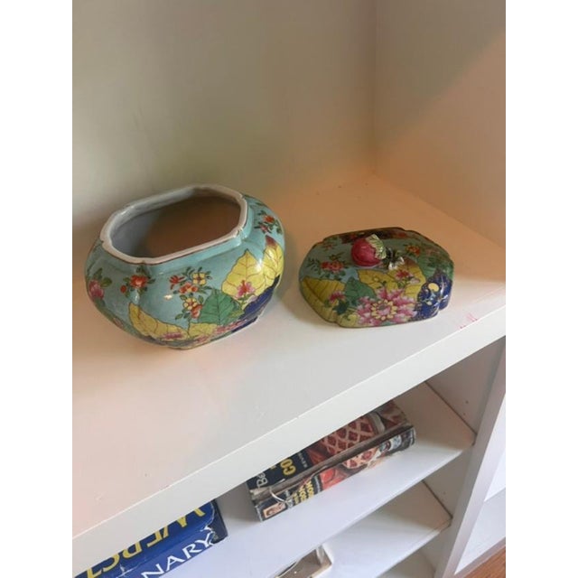 This is a vintage, hand-painted porcelain lidded jar featuring vibrant famille Rose style floral and leaf motifs on a...