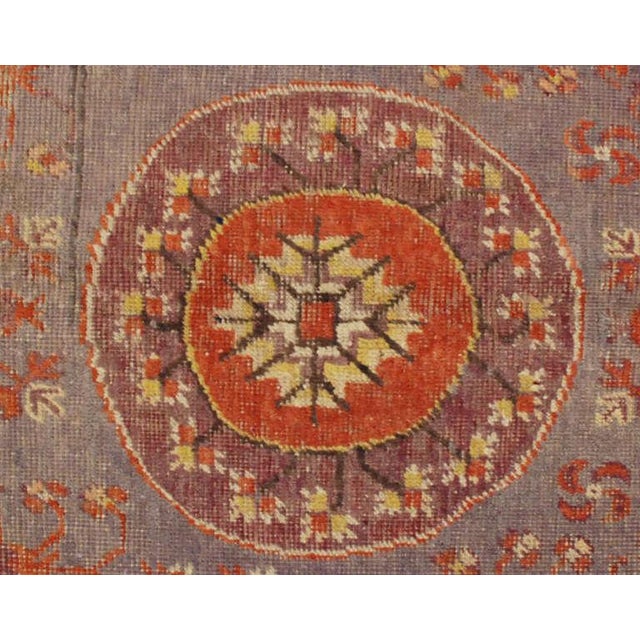 An antique Central Asian Khotan rug with asymmetrical central medallion amidst a field of flowers on a violet background,...