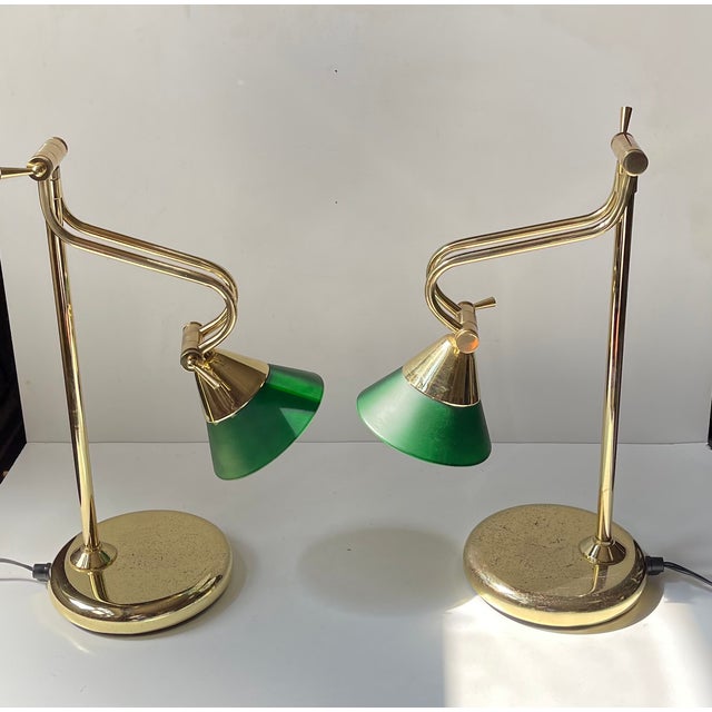 A pair of matching fully adjustable table or desk lights executed in solid brass and features cased green glass shades...