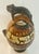 A dramatic hand-painted South American folk art pottery vessel featuring a sculptural jaguar handle gracefully arching...