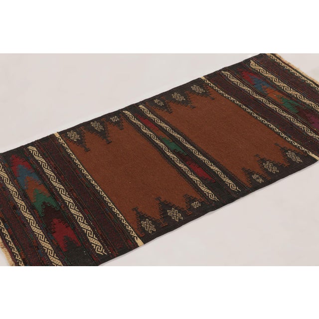 This 2x5 vintage Afghan runner, handwoven in wool circa 1950-1960, is a compelling example of tribal flatweave tradition....