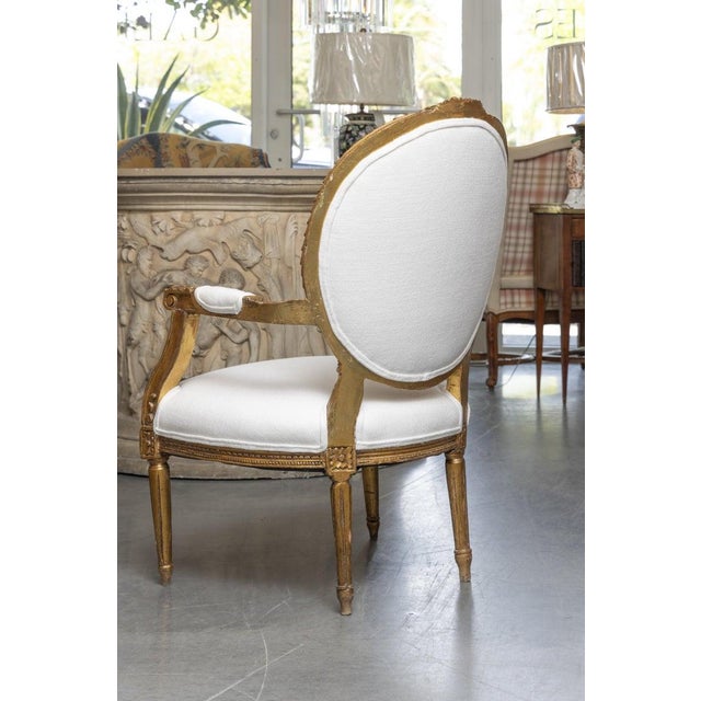 This is one of a pair of identical Louis XVI-style giltwood arm chairs with a gracefully shaped oval medallion back and...