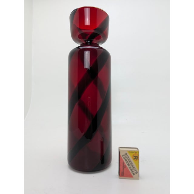 Ruby-red, mouth-blown cylindrical vase with spirally arranged black overlay stripes. Stelvia Glass was founded in the...