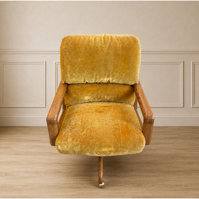 This vintage mid-century modern swivel-tilt armchair features textured mustard yellow upholstery and a wooden base with...