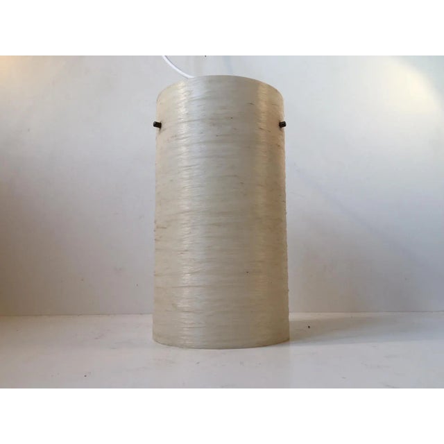 This cylindrical fiberglass pendant light with brass details was manufactured in Italy during the 1950s. It has a pastel...