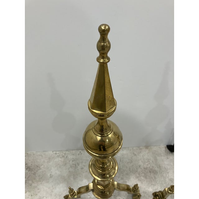 This pair of solid brass andirons is in the Federal style. The steeple top design is repeated in the miniature ones on the...