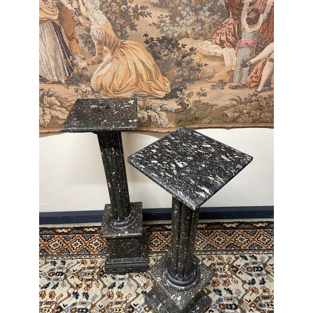 A striking pair of substantial black marble pedestal columns, featuring elegant brass accents and a decorative finish....