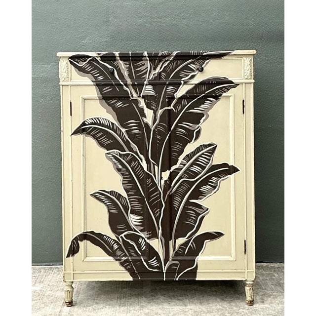 This vintage hand-painted cabinet brings bold tropical flair to any room with its striking banana leaf motif. Crafted from...