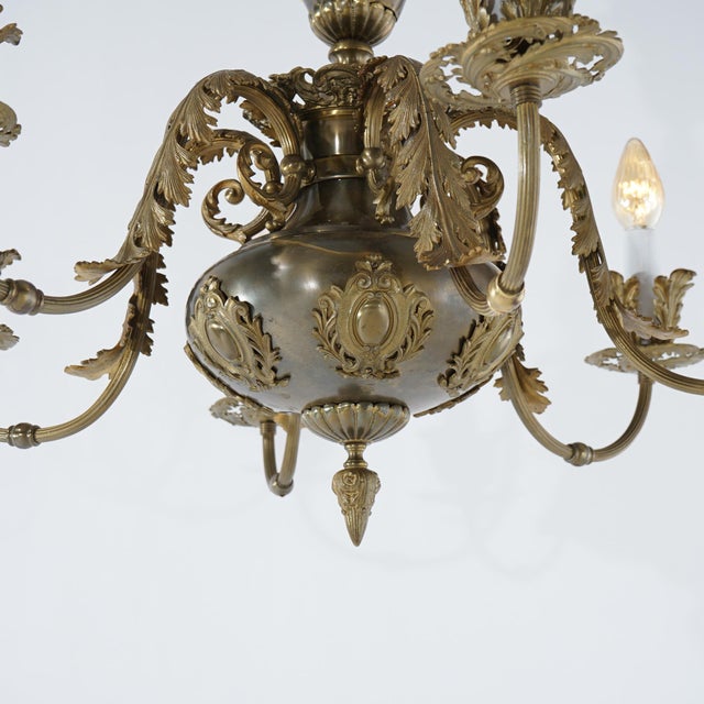 A large French Louis XV style chandelier offers brass and bronze construction with font having stylized shield form...