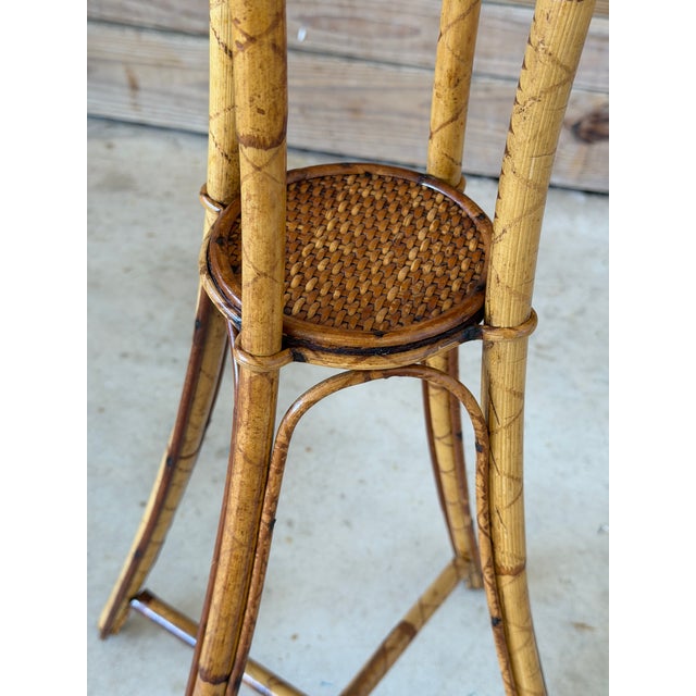 A charming pair of vintage faux bamboo plant stands featuring woven rattan tops and elegantly tapered tripod bases. The...
