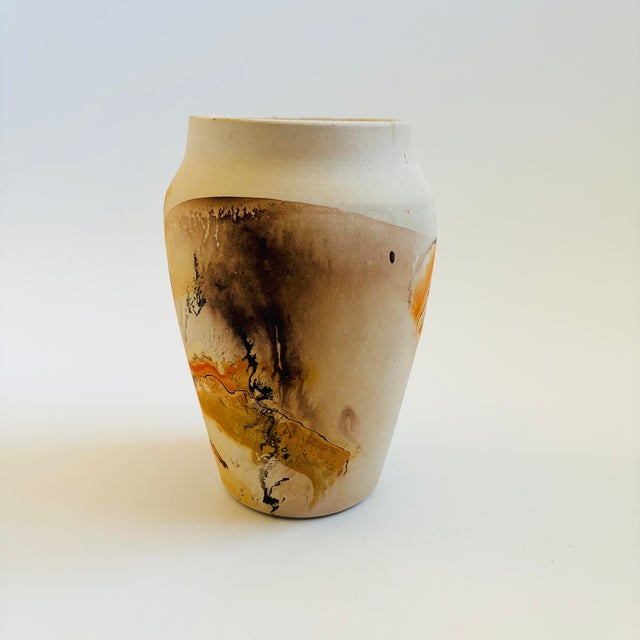 A vintage nemadji pottery vase with a beautiful organic pattern of orange and brown swirls on a light off-white...